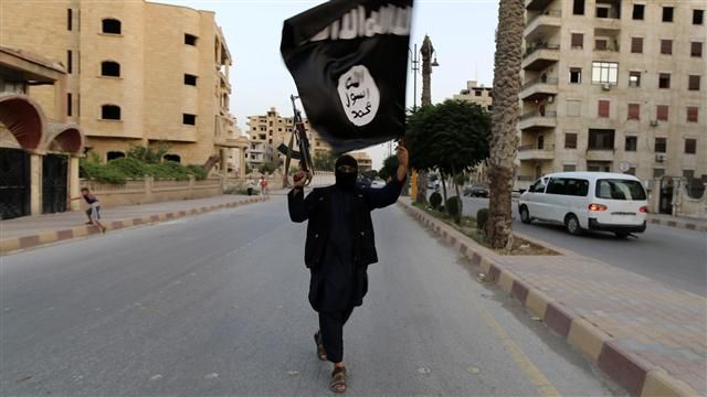 IS extremist brandishing the group’s flag and a weapon in Raqqa, Syria. 2014. (Ogbodo Solution/ Flickr Creative Commons)