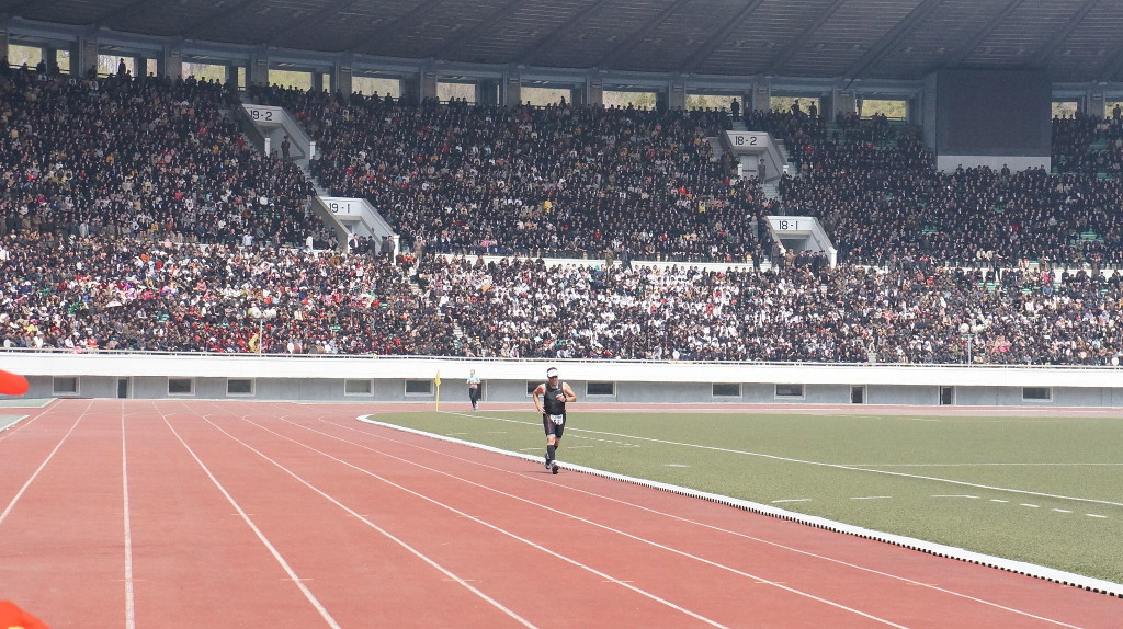 A runner enters a full stadium to finish the final lap of the 2014 Pyongyang Marathon. April 13, 2014 (Uri Tours/Wikimedia Commons)