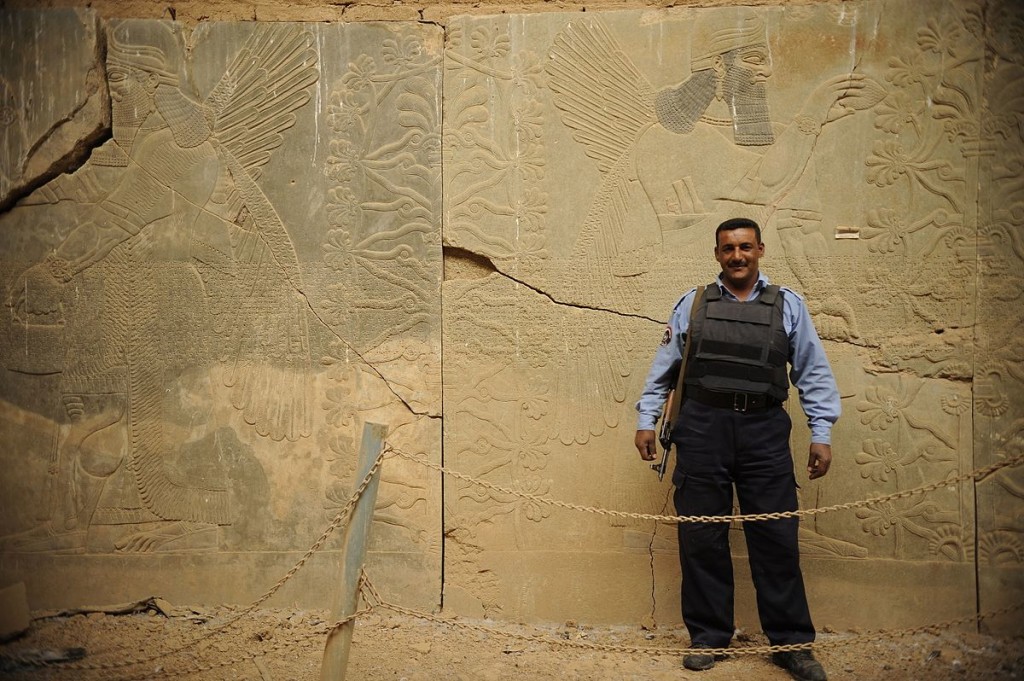 An Iraqi Policeman stands by a Nimrud wall relief that was protected by UNESCO prior to its destruction. 2008. (JoAnn Makinano/Wikimedia Commons)